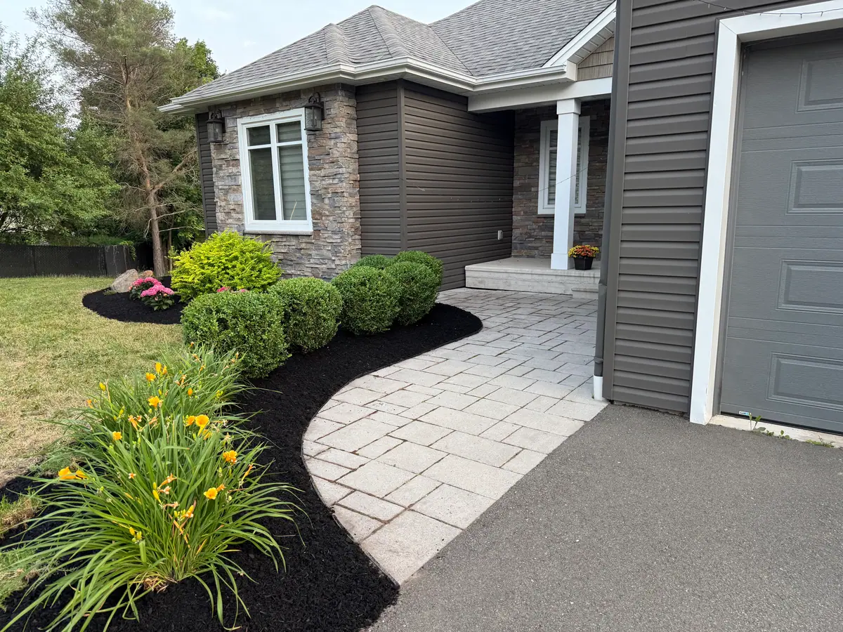 Curved paver walk to a front door, edged with black-mulched foundation beds of rounded shrubs and yellow daylilies