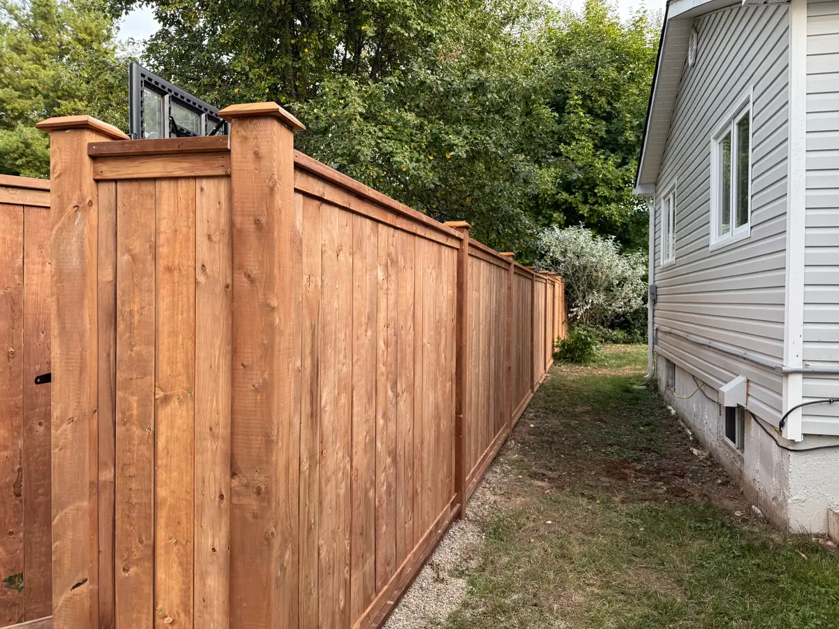 Tall wood board privacy fence with capped posts running along the side of a house