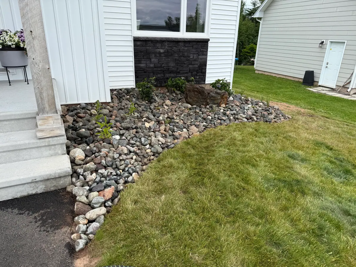 River-rock bed along a house foundation beside the front steps, with a curved edge to the lawn